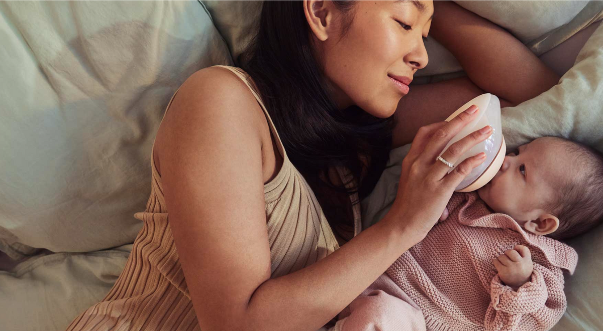 Mother feeding baby with a baby bottle shaped like a breast 